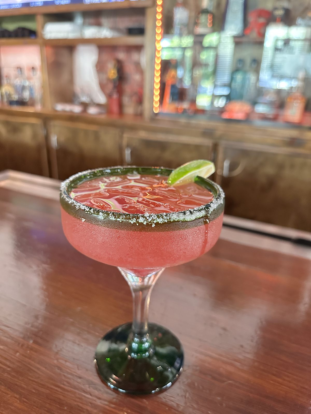 Frozen pink watermelon margarita in a salt-rimmed coupe against a moody backlit bar