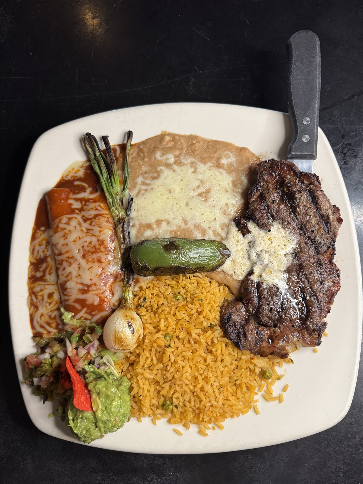 Grilled rib-eye steak with butter, cheese enchilada, cebollitas, rice, beans and guacamole
