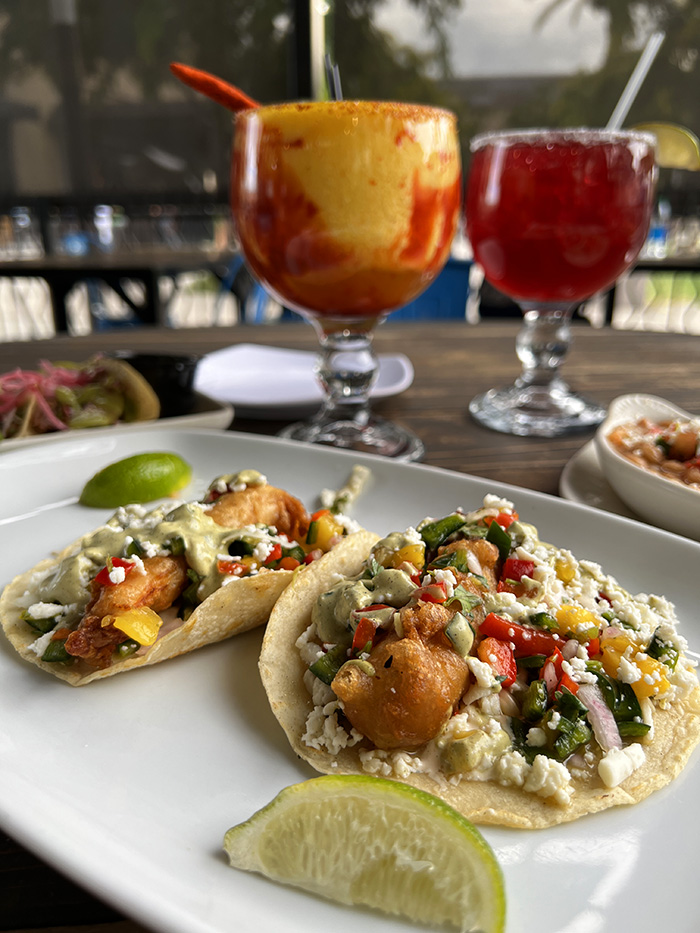 Two Baja-style seafood tacos with pickled slaw and lime, beside two frozen margaritas