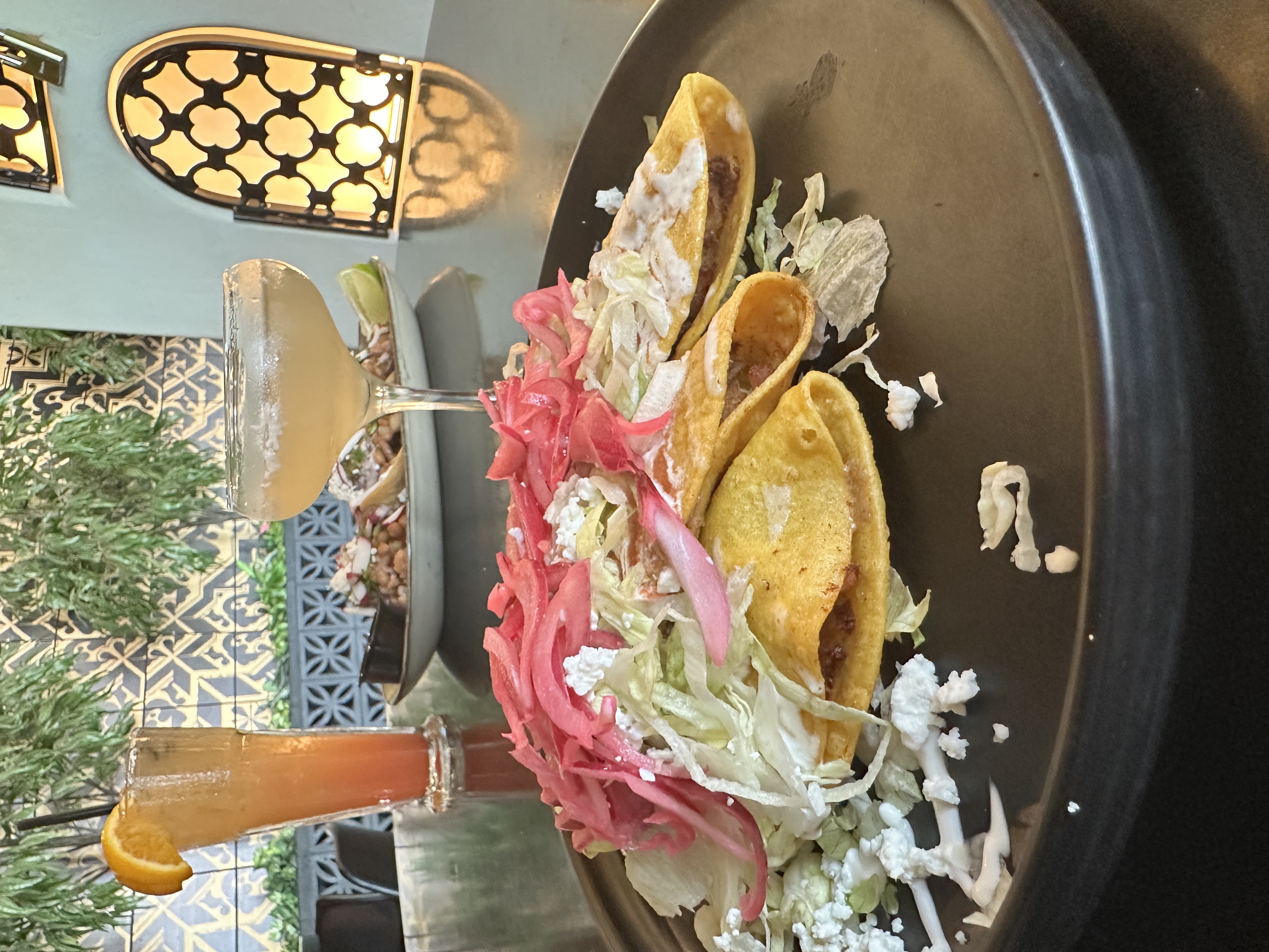 Three crispy tacos with pickled red onions and queso fresco, drinks alongside in the dining room